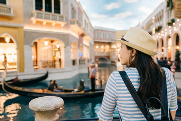 back view of elegant woman traveler with sunhat enjoy view to canal with passing by gondola in las...