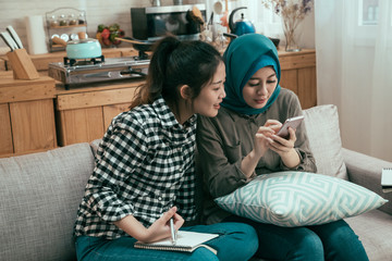 Concepts about technology communication and youth culture. Multiracial young people roommates relax at home kitchen sofa in day time. girl friends spending leisure time together using cellphone.