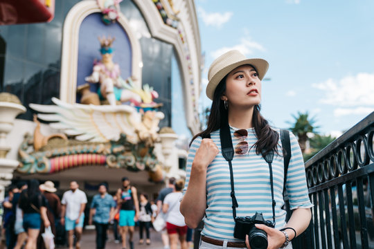 Young beautiful girl traveler walking in street outdoors on sunny day. elegant female photographer carry camera enjoy sunshine relax on las vegas boulevard with blue sky. bokeh view people in back