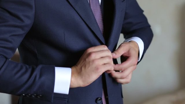 A man buttoning his jacket, close-up. A successful young man puts on a suit jacket in the morning. Businessman puts on a jacket.