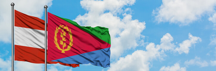 Austria and Eritrea flag waving in the wind against white cloudy blue sky together. Diplomacy...