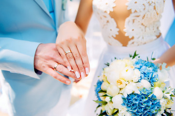 Obraz na płótnie Canvas Hands of newlyweds with beautiful gold rings, close-up. White bridesmaid dress, bouquet, stylish manicure. Perfect wedding ceremony.