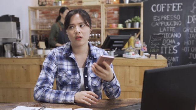 stressful college girl angry and mad at smartphone in cafe. student discussing on cellphone disagree with teamwork partner on project hang up phone and typing message. waitress make coffee in counter