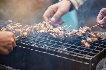 People standing toast, grilled chicken and pork on the stove with smoke in the celebration.