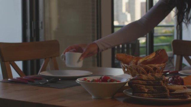 Female serving breakfast table with coffee, bread, strawberries, coffee. Table with skyline view.