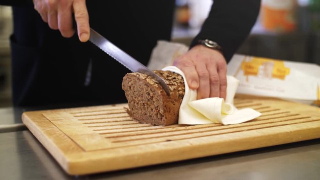 4K Slow motion close up of a a fresh whole-grain bread being sliced with a knife. Grains falling of the loaf, filmed with a wide aperture