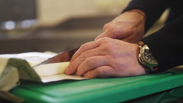 4K Slow motion close up of a a fresh cheese being sliced with a knife. Slight camera pan, filmed with a wide aperture
