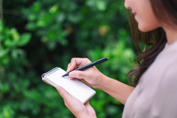 Closeup image of a woman holding and writing on blank notebook in the outdoors