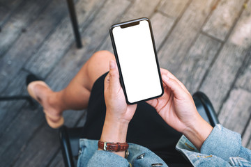 Top view mockup image of a woman holding a black mobile phone with blank white desktop screen