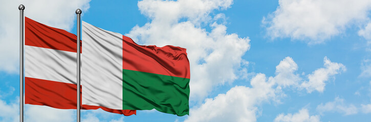 Obraz premium Austria and Madagascar flag waving in the wind against white cloudy blue sky together. Diplomacy concept, international relations.