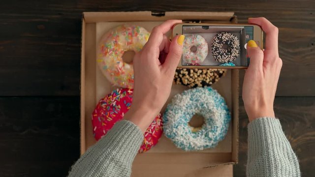 Top view of Woman hands taking a photos of sweet tasty donuts in box. Food by smartphone close-up.