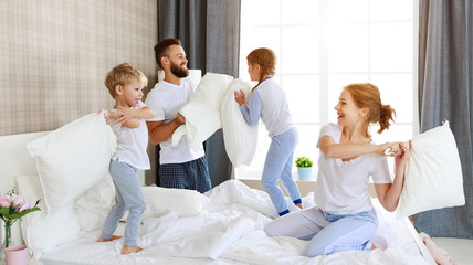 happy family mother, father and children laughing, playing and jumping in bed   at home