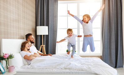 Obraz na płótnie Canvas happy family mother, father and children laughing, playing and jumping in bed at home