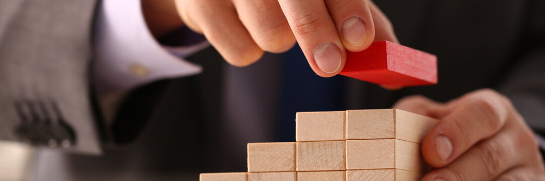 Male hand holds red wood block of stair