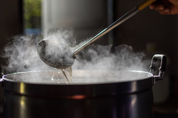 Cooking person in the restaurant is cooking while using the dipper in a large pot. And the water is boiling.