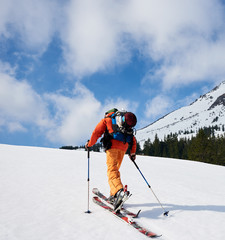 Back view of ski mountaineer walking up along snowy ridge with the skis in the backpack. In background a blue sky. Snow and winter activities, skitouring in mountains.