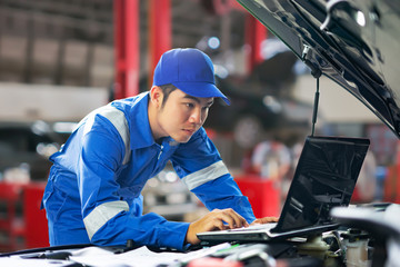 car service, repair, maintenance  concept - auto mechanic man or Smith writing to the clipboard at warehouse workshop, technician doing the checklist for repairs engine a car in the garage with laptop