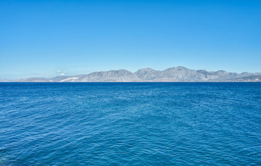 Fototapeta na wymiar Calm azure Mediterranean Sea and mountain in horizon. Silhouettes landscape on Greek island Crete.