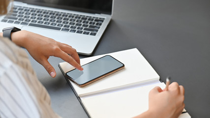 Cropped shot young woman working with smartphone on table.