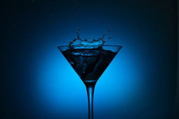 cocktail glass with blue alcoholic drink splashing out, close-up. 