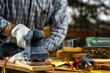 Adult carpenter craftsman wears protective leather gloves, with the electric sander smoothes a wooden table. Construction industry, housework do it yourself. Stock photography.