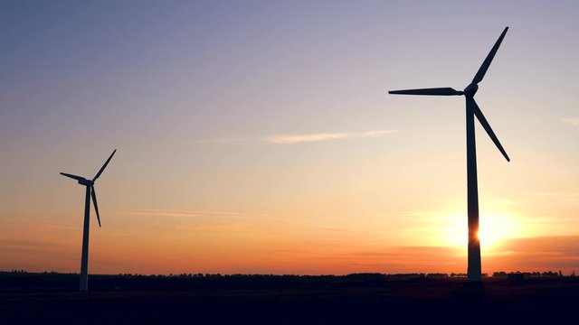 Sunset above the windmills silhouette on the field
