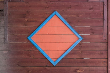 A wooden gate made of old faded red boards with an orange square in the middle and iron hinges at the edges. Blue slats on the border of the orange square. Door hinges with bolts.