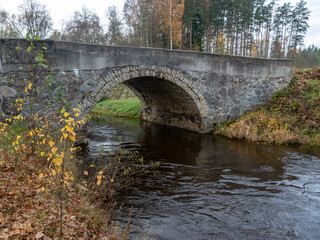 Fototapeta na wymiar beautiful stone arched bridge over the small river, autumn day