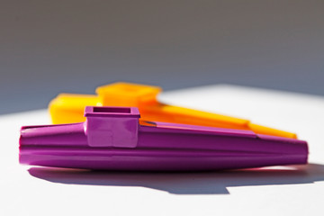 a purple and a yellow musical instrument is located on a sunny window sill, Kazoo