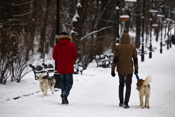 Fototapeta na wymiar two friends walking by snowed city park with husky dogs