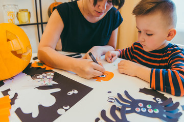 young mother with toddler son making craft spiders for halloween holiday