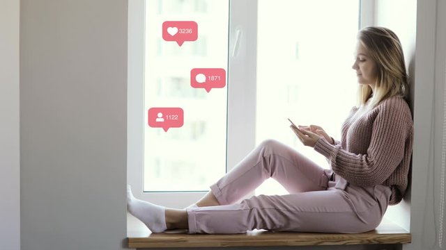 Girl blogger sitting on window and browsing phone, side view. Indicators with likes, comments and followers, rising counters of social network account near her. Concept of modern work in social media.