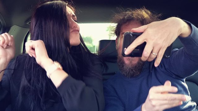 Funny couple making video with smartphone while dancing having fun in car taxi closeup