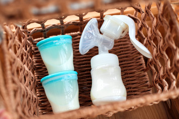 Breast pump and containers with breast milk for baby in straw basket. Maternity and baby care concept. Top view. - 297497196