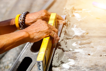 Closeup hands of laborer holding a building level working at construction site with sun flare background.