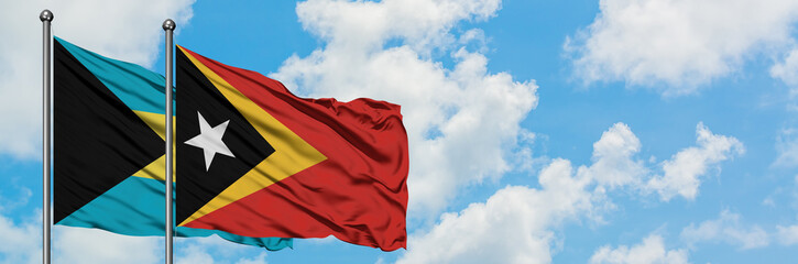 Naklejka premium Bahamas and East Timor flag waving in the wind against white cloudy blue sky together. Diplomacy concept, international relations.