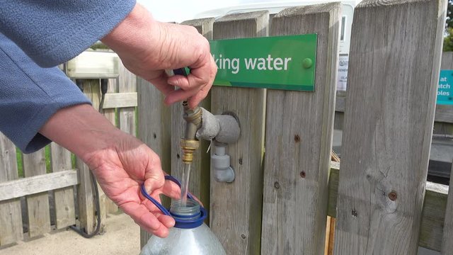 Close POV shot of a man’s hands filling a plastic container at the drinking water tap on a campsite.