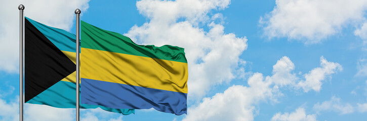 Bahamas and Gabon flag waving in the wind against white cloudy blue sky together. Diplomacy...