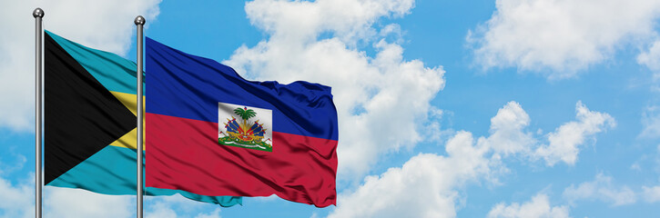 Naklejka premium Bahamas and Haiti flag waving in the wind against white cloudy blue sky together. Diplomacy concept, international relations.