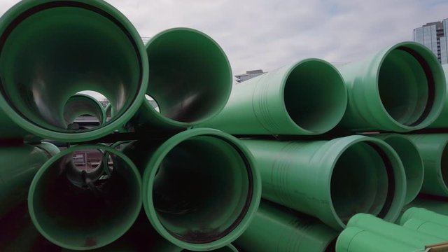 Organically panning perpendicularly to large green stacked PVC pipes while peering through the other side.