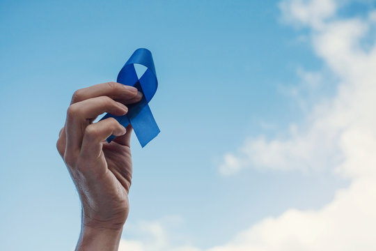 Man Hands holding blue ribbon over blue sky, Prostate Cancer Awareness, November blue, Movember Men health awareness
