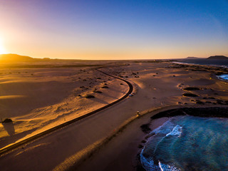 Beautiful aerial view of coast beach during the sunset -blue ocean and yellow sand and desert with sun light come from montains in background -travel and vacation concept