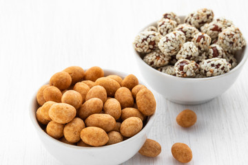Peeled peanuts and peanuts in syrup with sesame seeds lie in two white bowls on a white wooden background