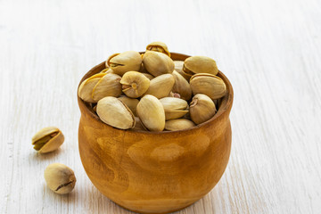 Pistachios lie in a brown wooden bowl on a white wooden background, top view from the side