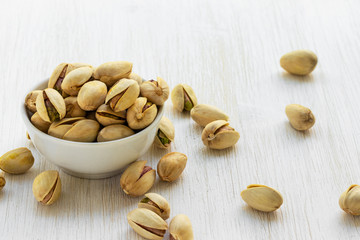 Pistachios lie in a white glass bowl on a white wooden background, top view from the side