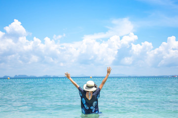 The image behind the woman raise their arms and a hat In the sea background sky and cloud.