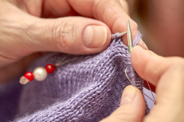 Woman is knitting a blue warm sweater. A hobby of elderly woman is knitting. Closeup view of knitting loop. Selective focus