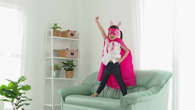 Little asian girl in superhero costume with mask playing in living room 