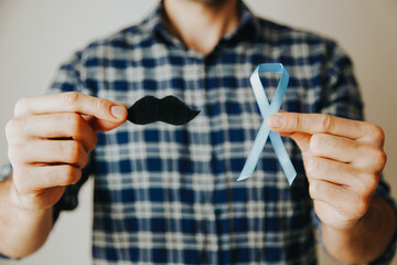 Man 's hands holding a blue ribbon and moustache in front of him. Prostate cancer awareness month....
