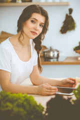 Young woman looking for a new recipe for cooking in a kitchen. Housewife is making online shopping by tablet computer and credit card